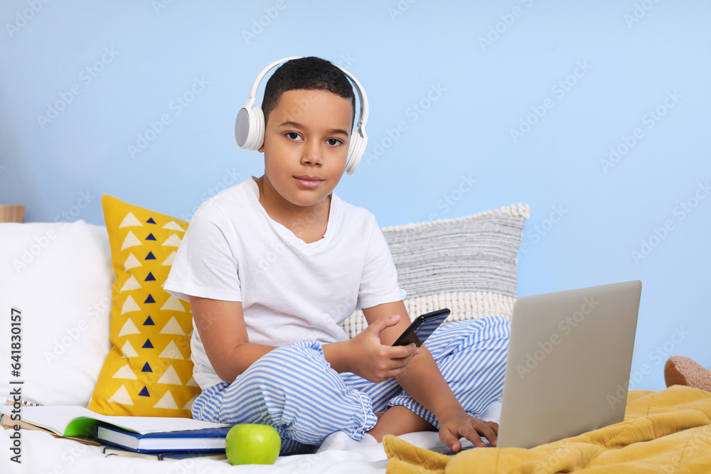 Little African-American boy with laptop studying computer sciences online in bedroom