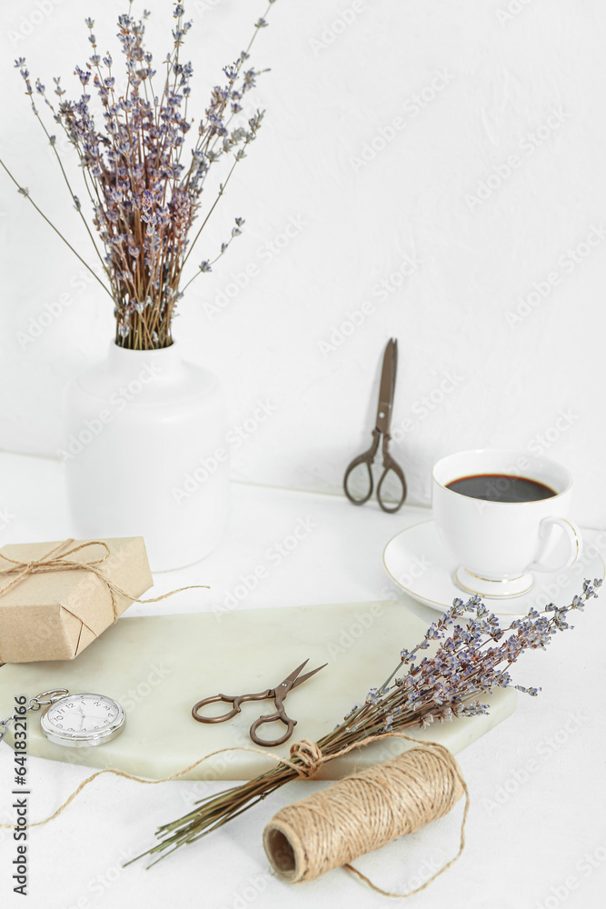 Cup of coffee with scissors, thread and dried lavender on white table near wall