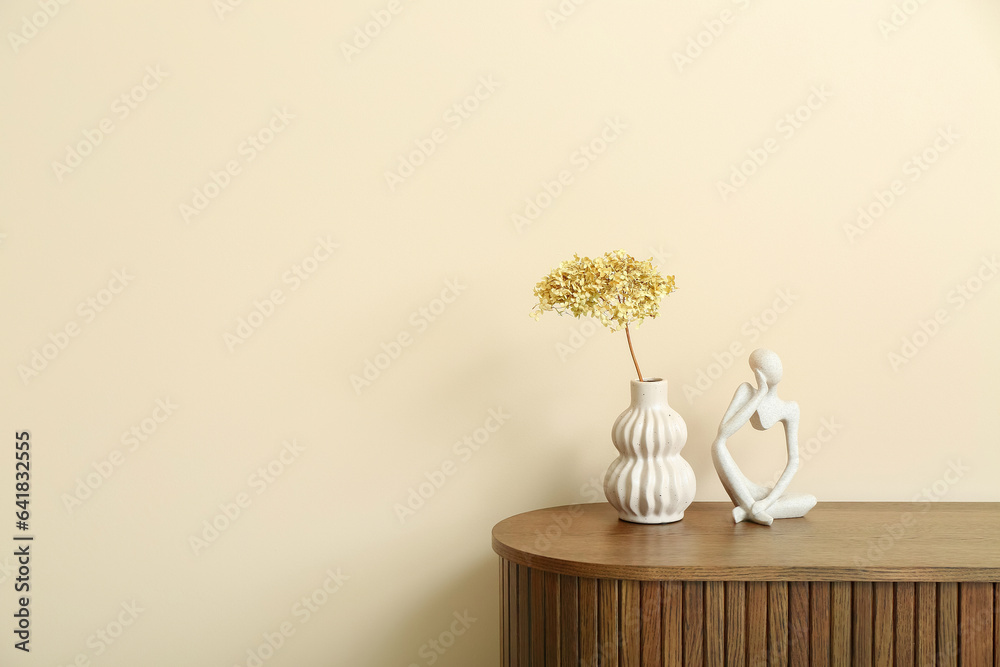 Vase with dried hydrangea and figurine on dresser near beige wall