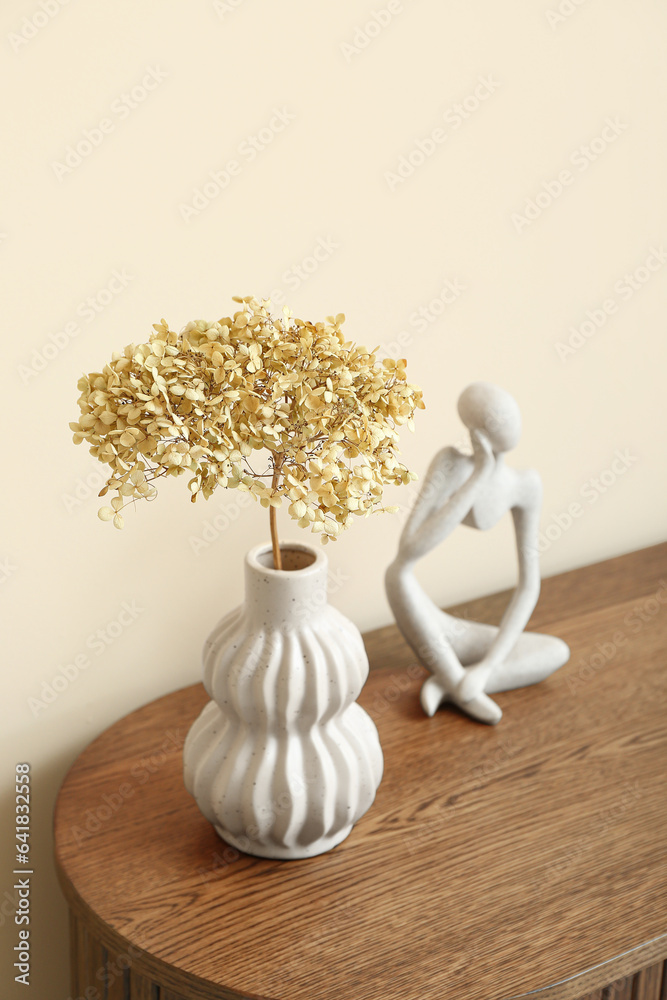 Vase with dried hydrangea and figurine on dresser near beige wall