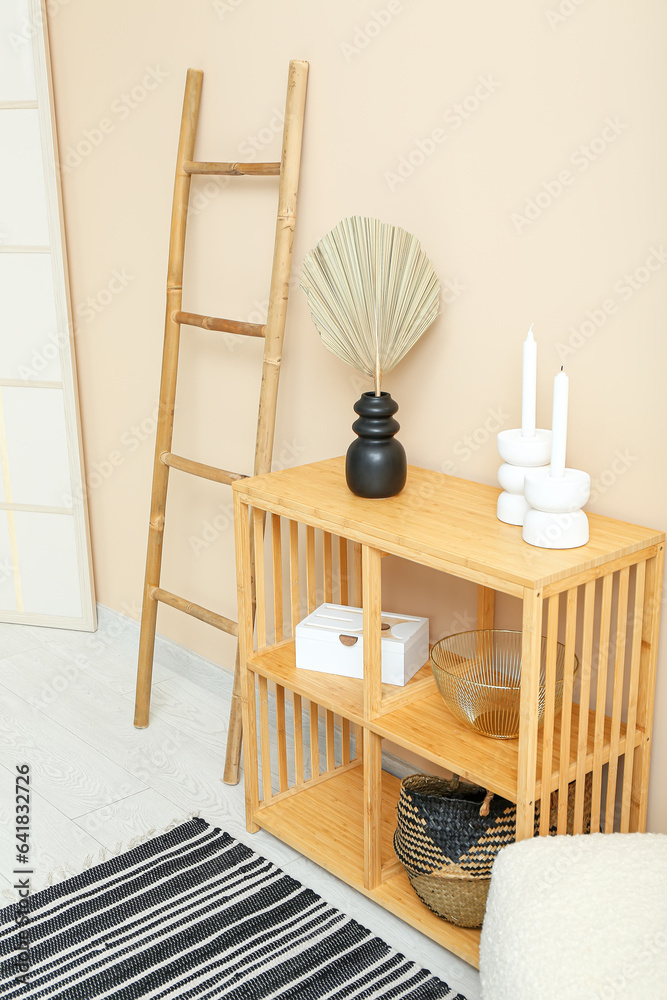 Vase with dried palm leaf, dresser and ladder near beige wall