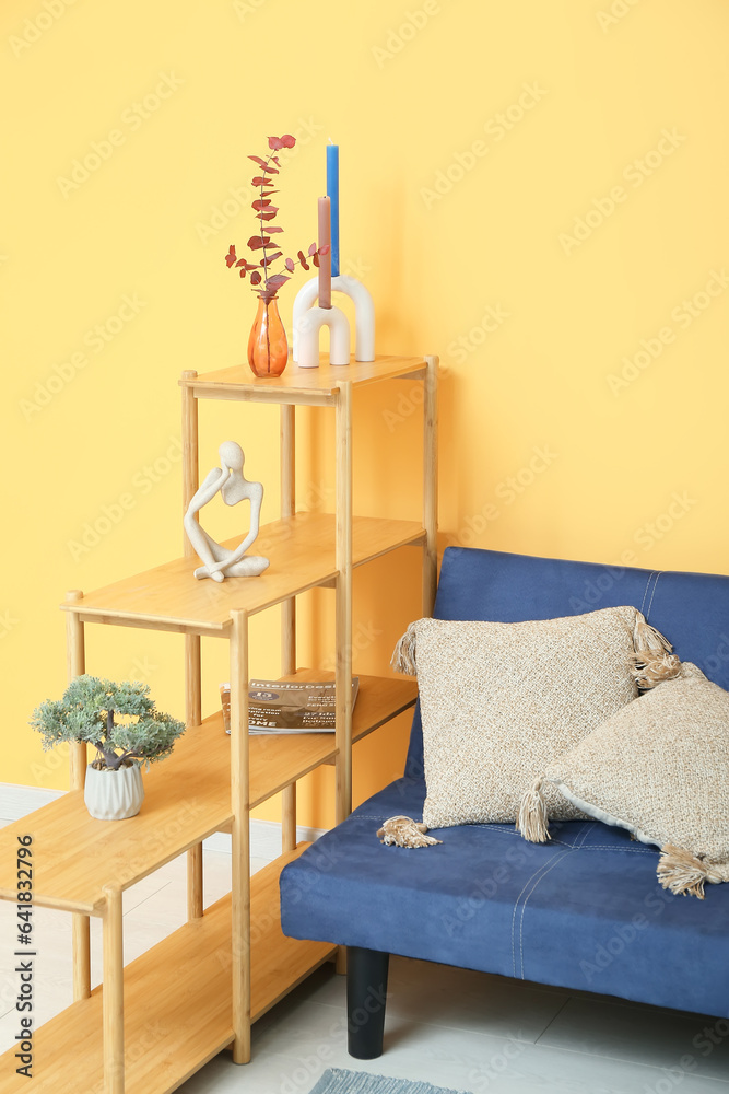 Vase with dried red leaves twig, shelving unit and couch near yellow wall