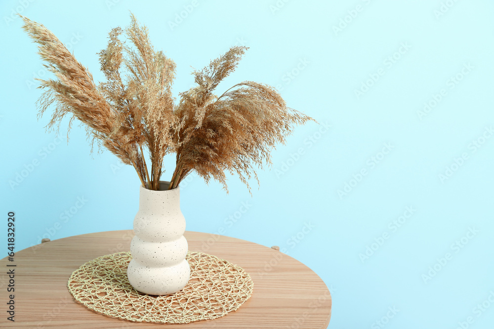 Vase of dried pampas grass with figurine on coffee table near blue wall