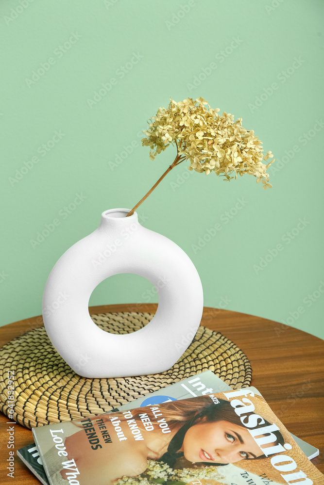 Vase with dried hydrangea, magazine and mat on coffee table near green wall