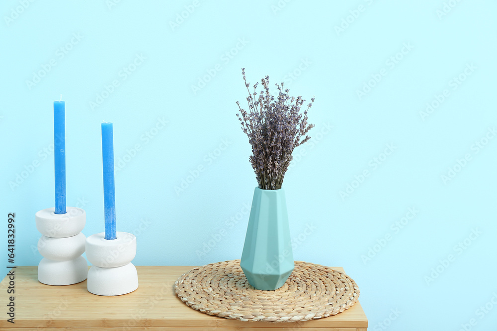 Vase with dried lavender, mat and candles on shelving unit near blue wall