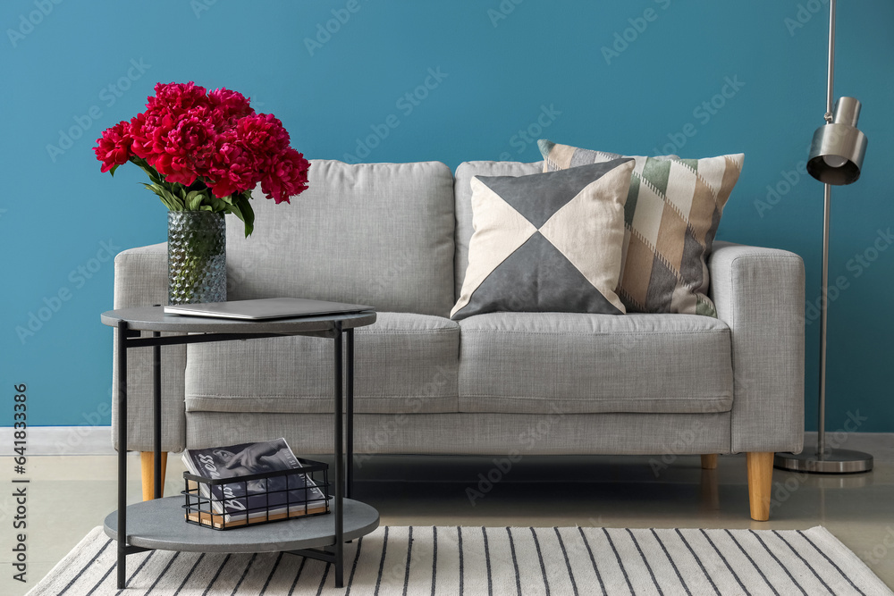 Vase of red peonies with coffee table, couch and floor lamp near blue wall