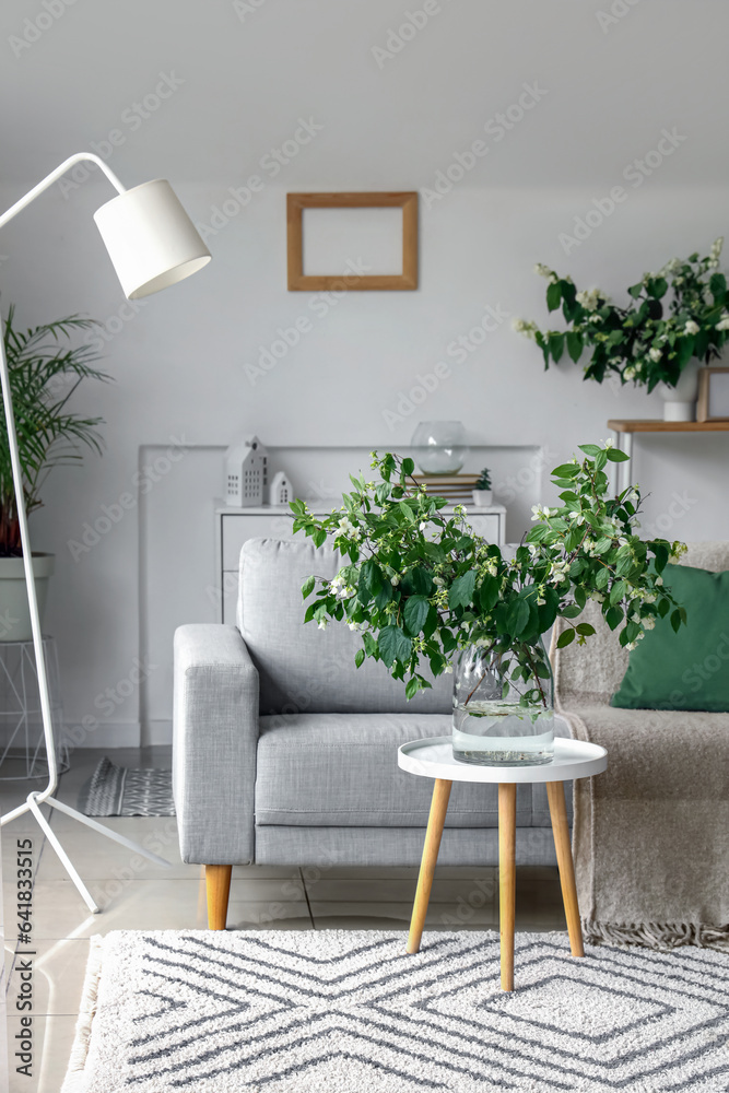 Grey sofa and vase with blooming jasmine flowers on coffee table in living room