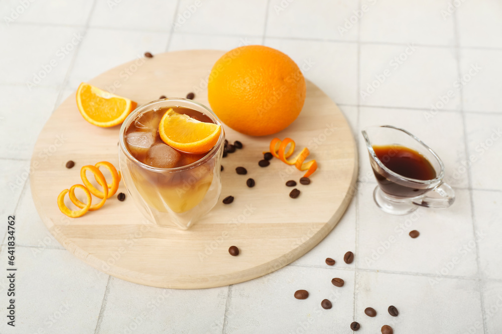 Glass of tasty orange espresso and ingredients on white tile background