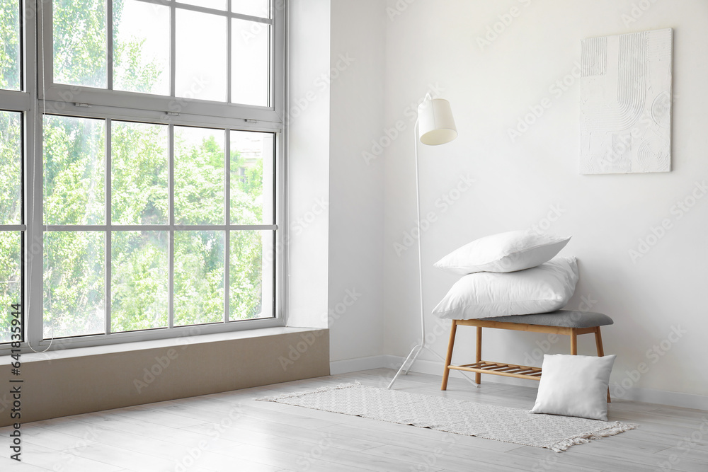 Grey bench with pillows and standard lamp near white wall