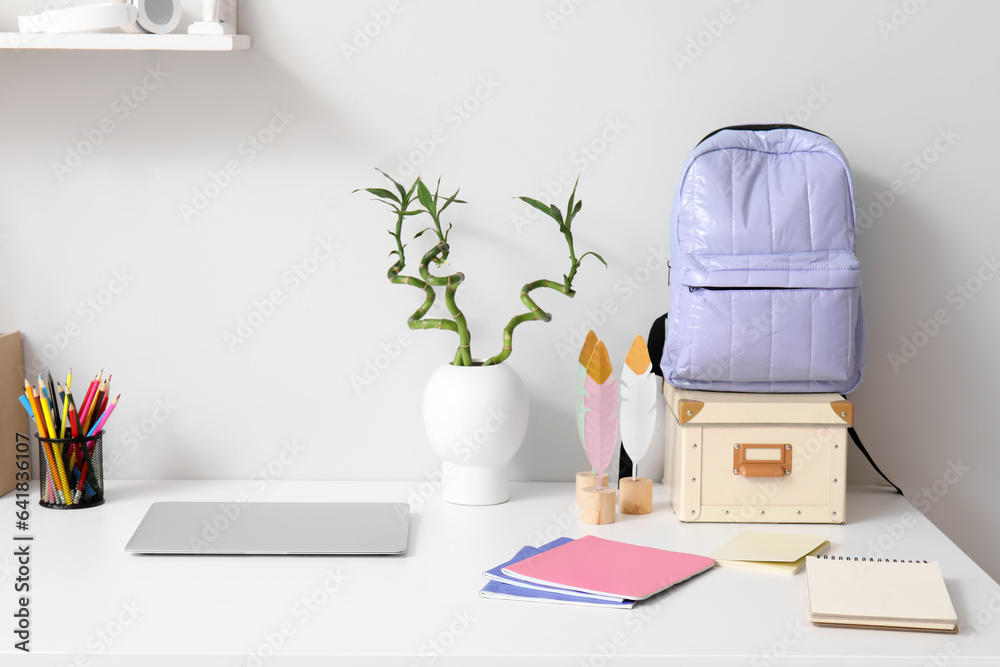 Modern school desk with laptop and stationery in room near white wall