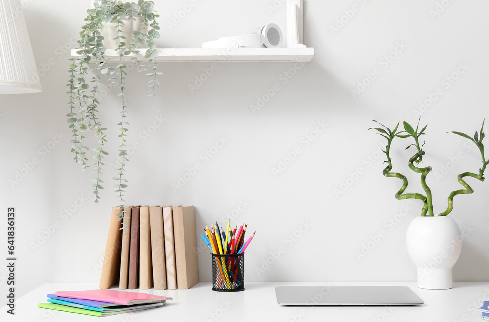 Modern school desk with laptop and stationery in room near white wall