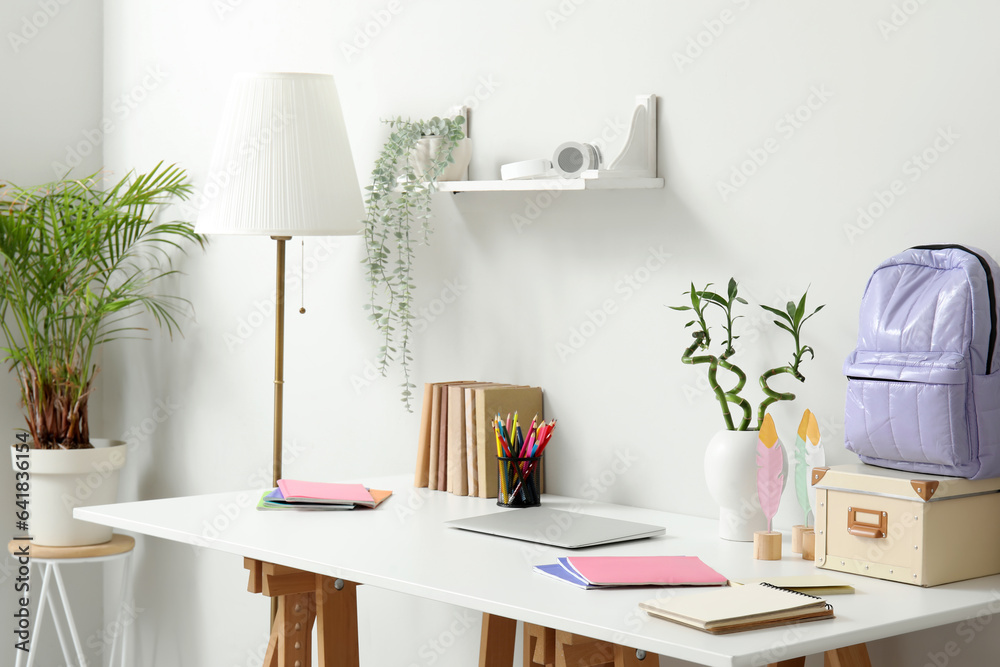 Modern school desk with laptop and stationery in room near white wall