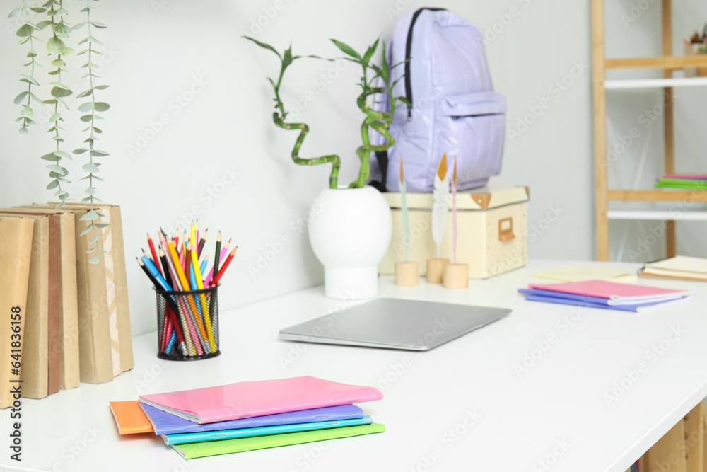 Modern school desk with laptop and stationery in room near white wall