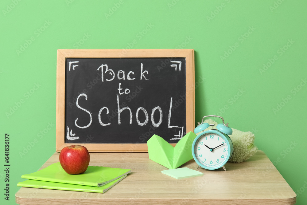 Modern school desk, stationery and blackboard with text BACK TO SCHOOL in room near green wall