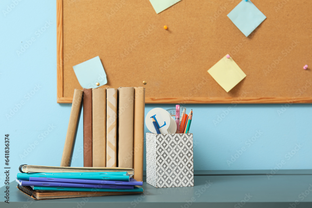 Modern school desk with stationery and cork board in room near blue wall