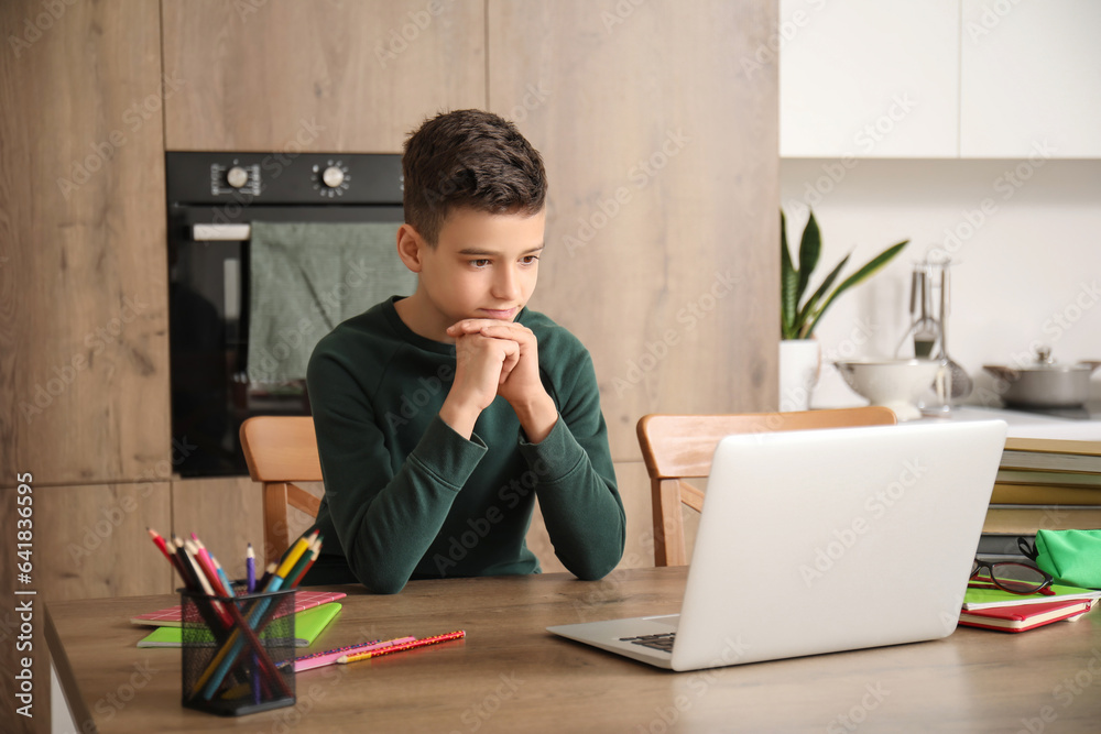 Little boy studying online with laptop in kitchen