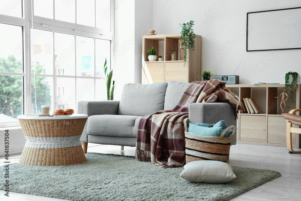 Modern living room interior with grey sofa, coffee table, blanket and wicker basket