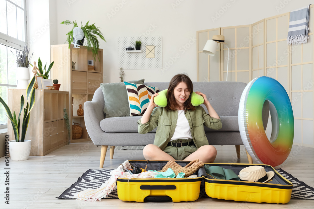 Young woman unpacking neck pillow from suitcase at home