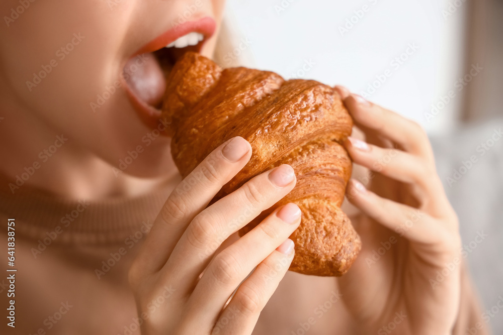 Beautiful young woman eating tasty croissant in living room, closeup