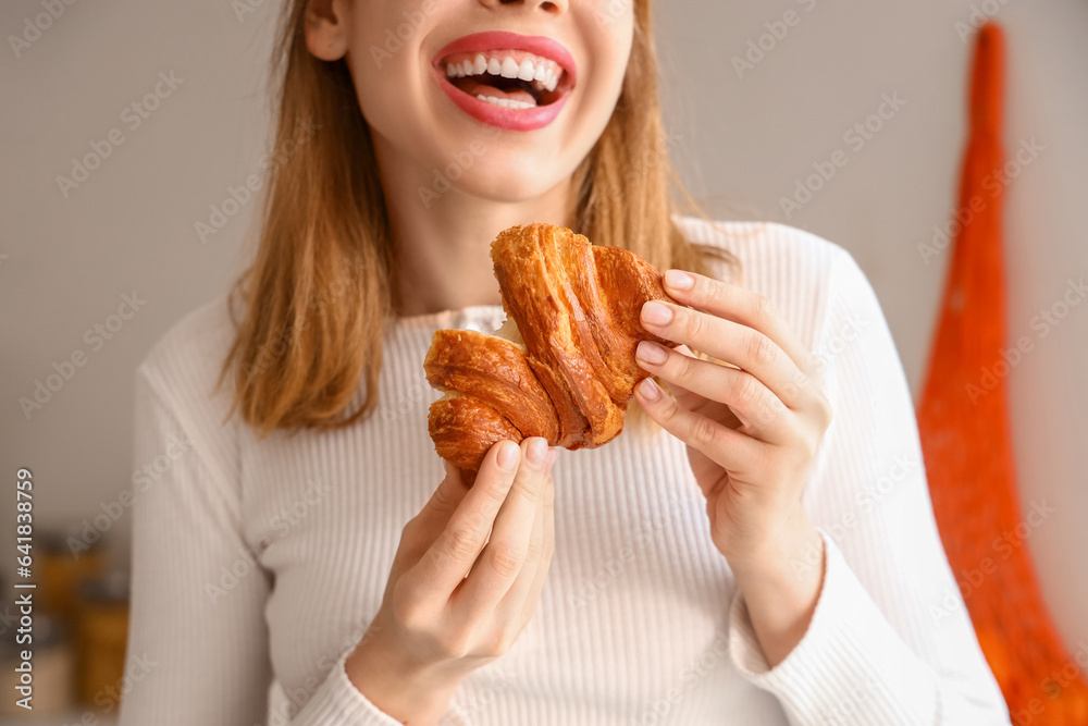 Beautiful happy young woman with tasty croissant in kitchen