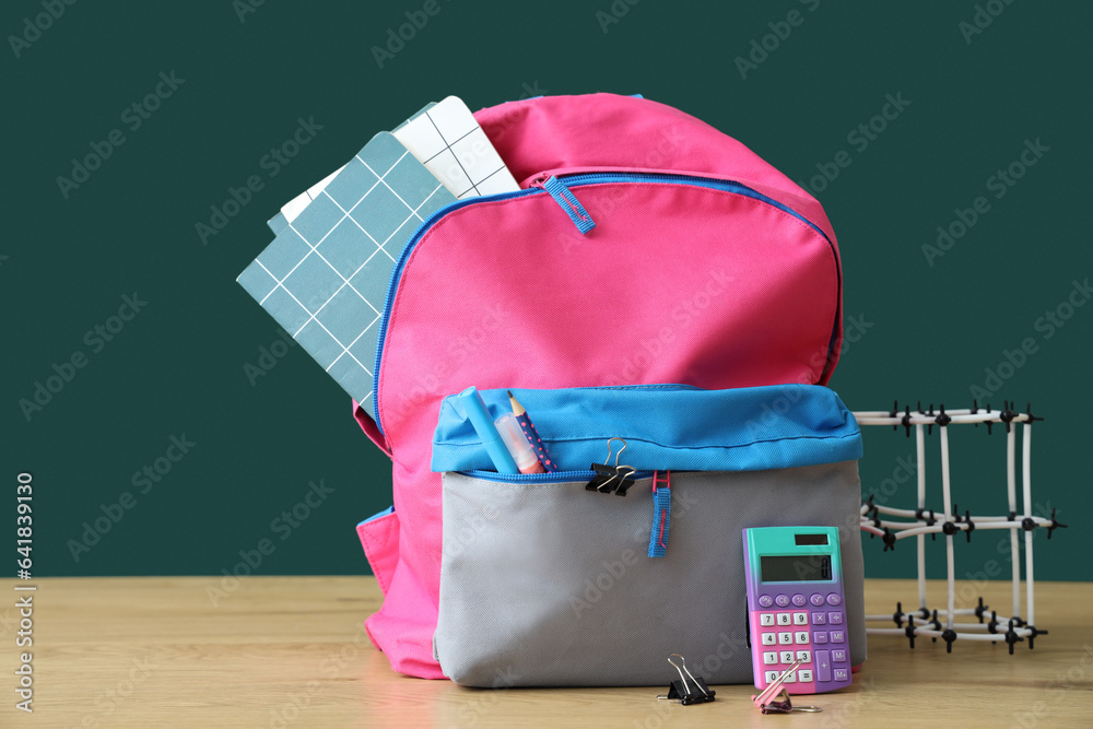 Backpack with school stationery and molecular model on table near green chalkboard