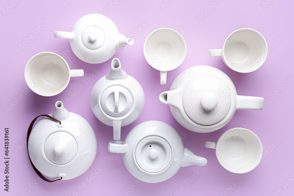 Many porcelain teapots and cups on lilac background