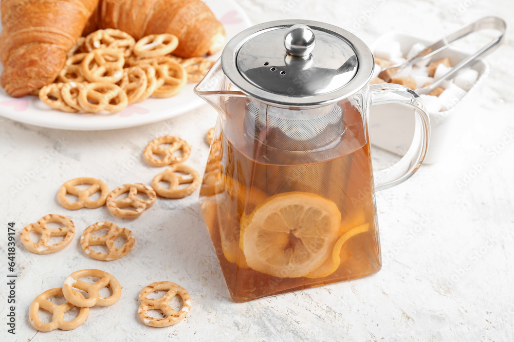 Glass teapot with tasty lemon tea and snacks on white table, closeup