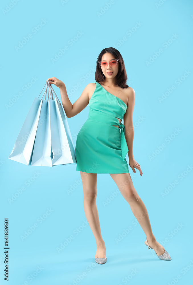 Beautiful stylish young Asian woman with shopping bags on blue background