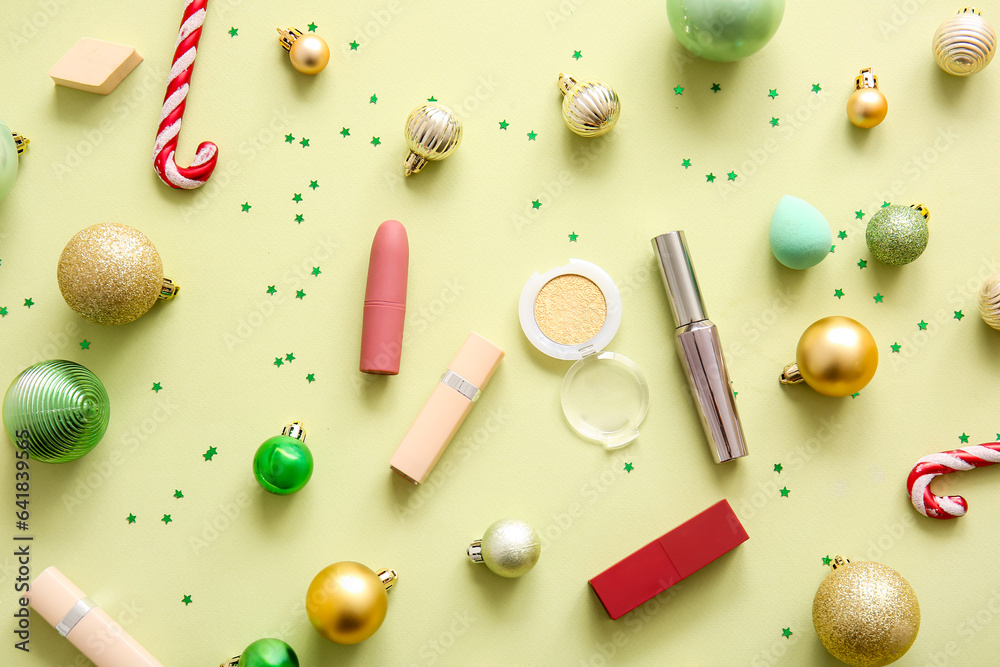 Composition with decorative cosmetics and Christmas decor on light yellow background