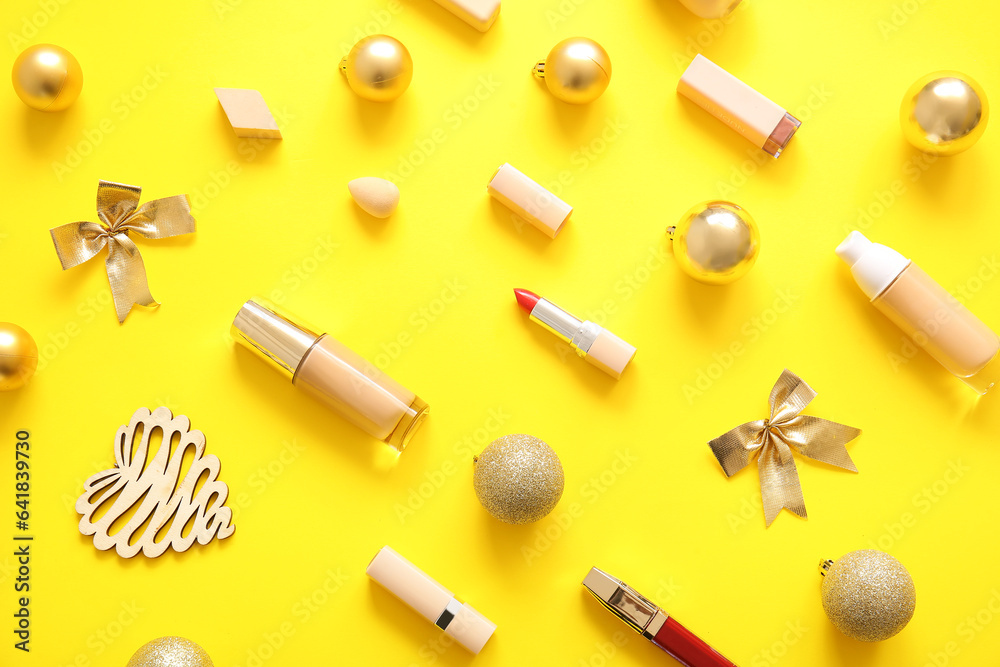 Beautiful makeup products and golden Christmas decor on yellow background