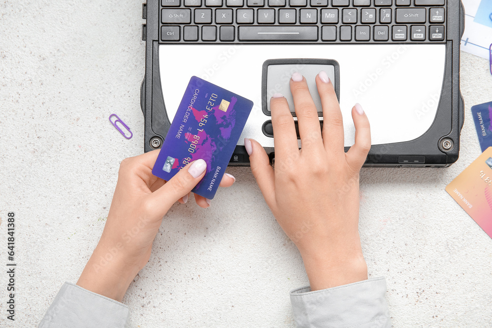 Woman with credit card using old laptop at white table