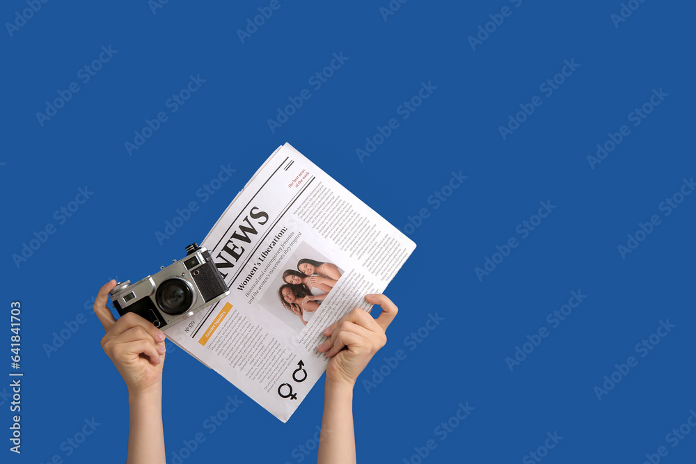 Female hands with newspaper and photo camera on blue background