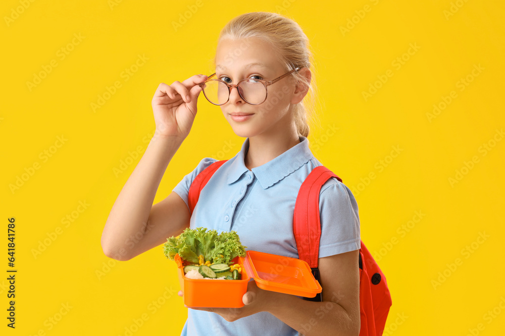 Girl in eyeglasses with backpack and lunchbox on yellow background