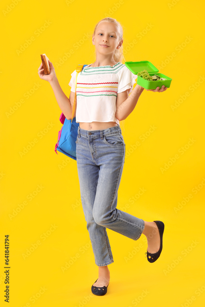 Happy girl with backpack, lunchbox and sandwich on yellow background