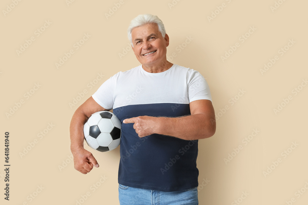 Mature man pointing at soccer ball on beige background