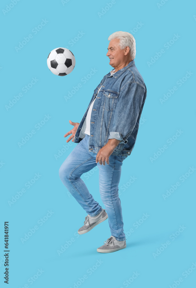 Mature man playing with soccer ball on blue background