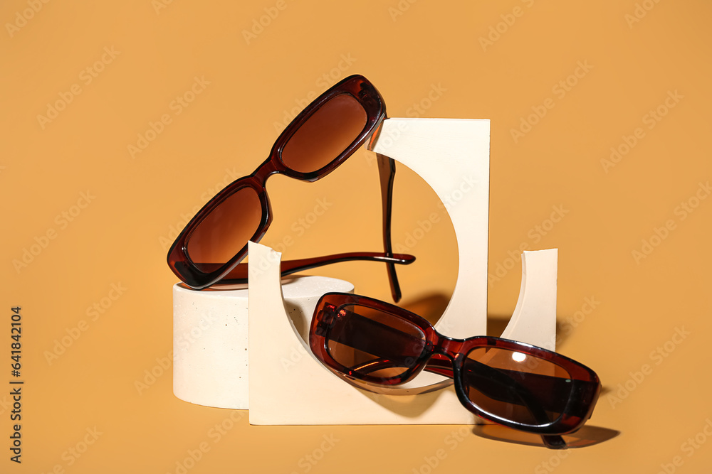 Stands with different stylish sunglasses on orange background