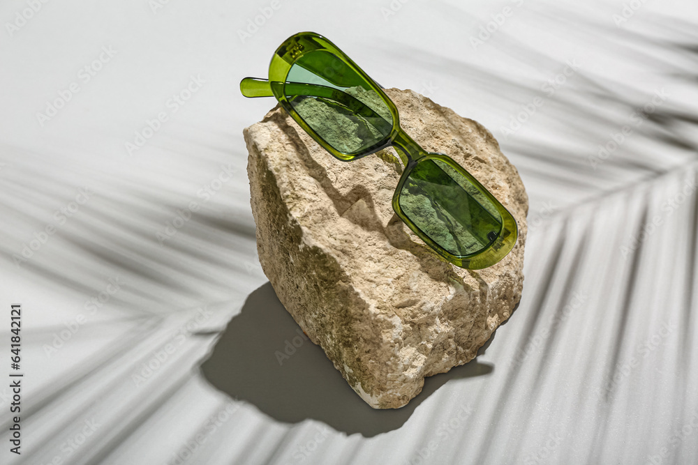 Stone with stylish modern sunglasses on grey background