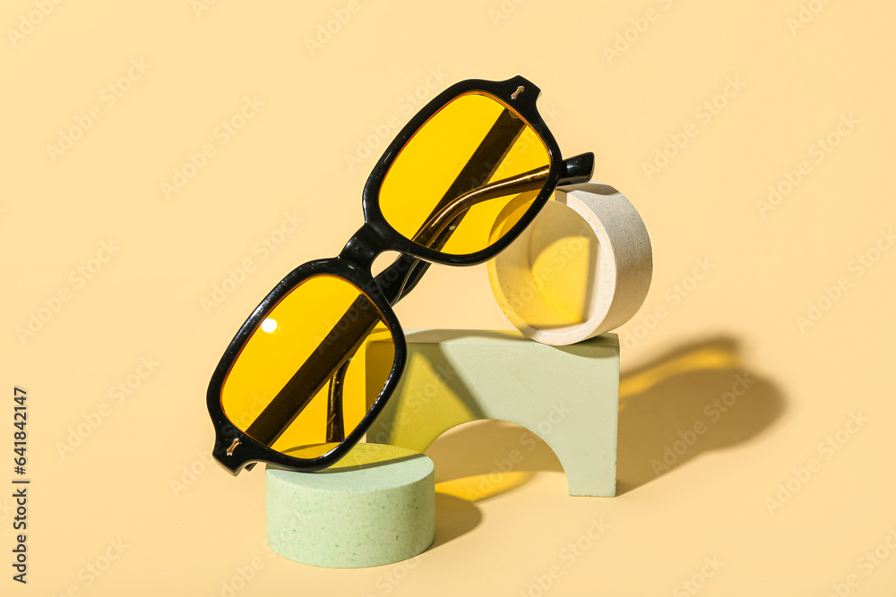 Stands with stylish sunglasses on pale yellow background