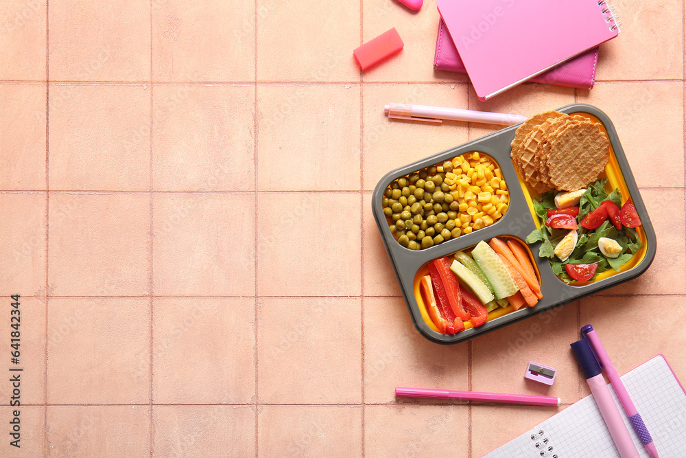 Lunchbox with delicious food and different stationery on orange tile background