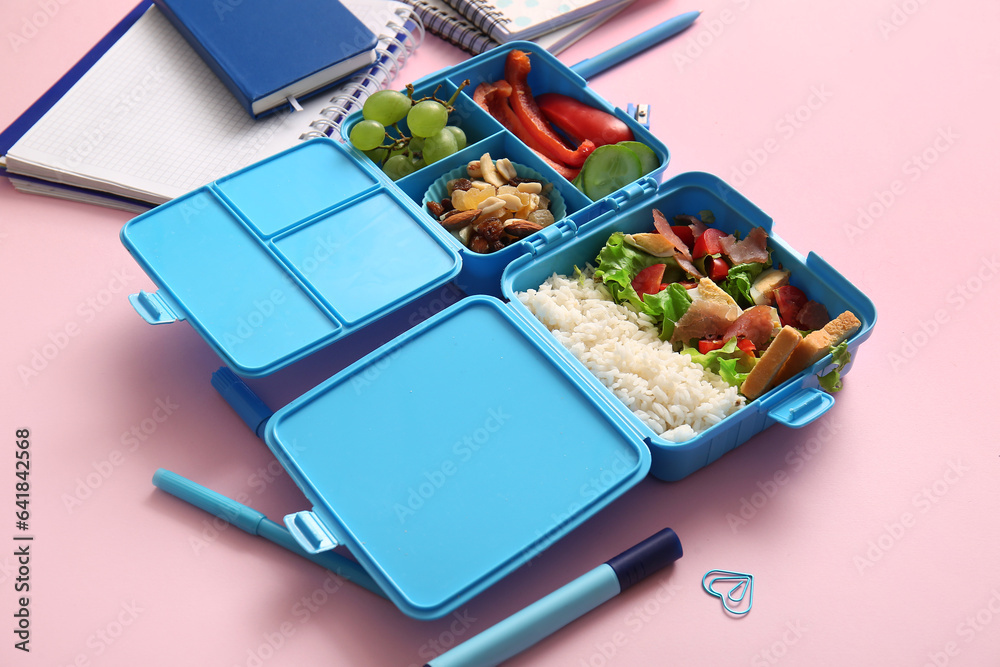 Lunchbox with delicious food and different stationery on pink background