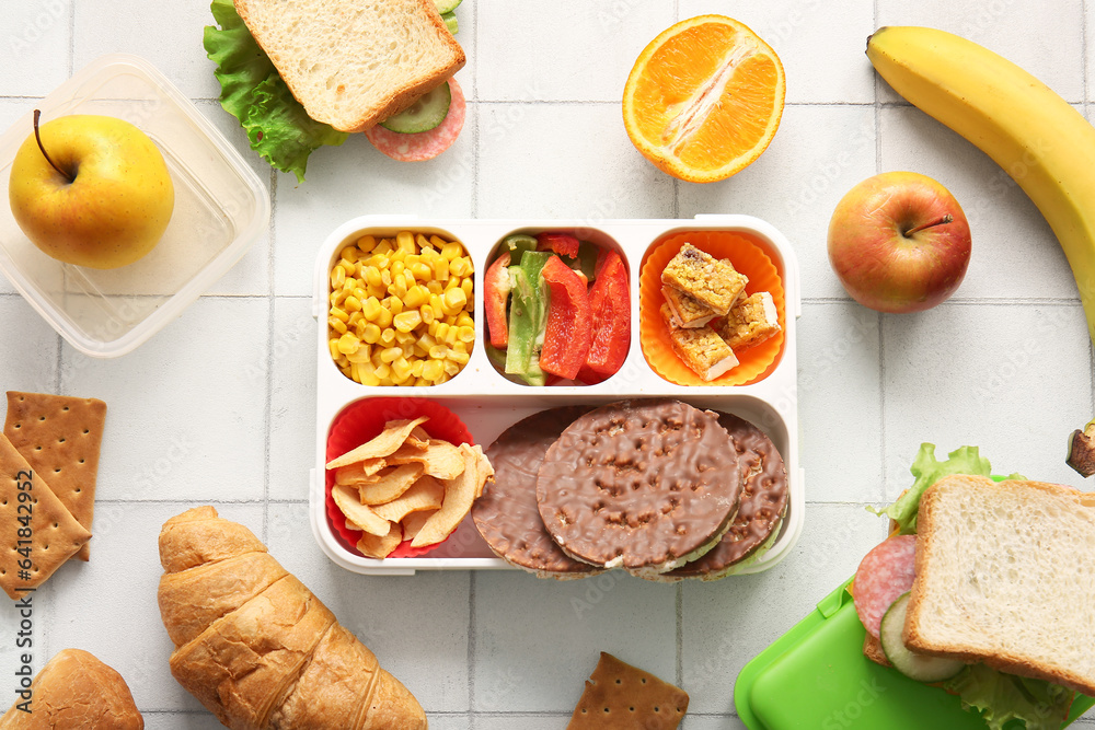 Lunchboxes with different delicious food on white tile background