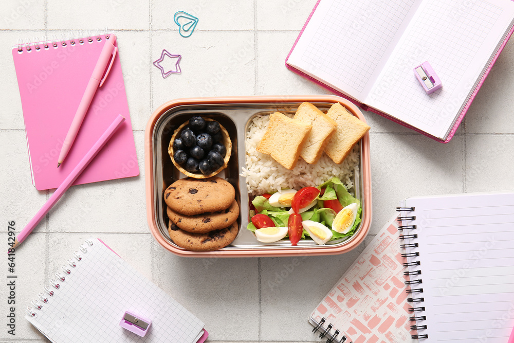 Lunchbox with delicious food and different stationery on white tile background