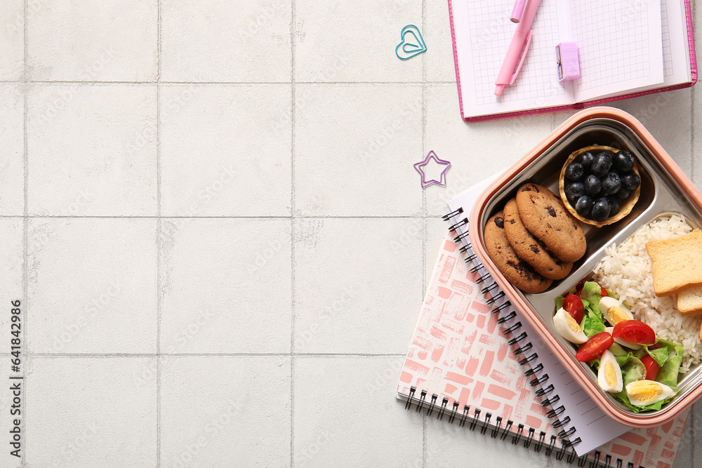 Lunchbox with delicious food and different stationery on white tile background