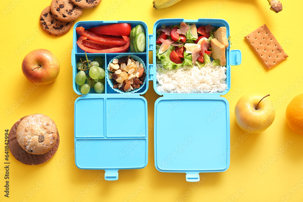 Lunchboxes with different delicious food on yellow background