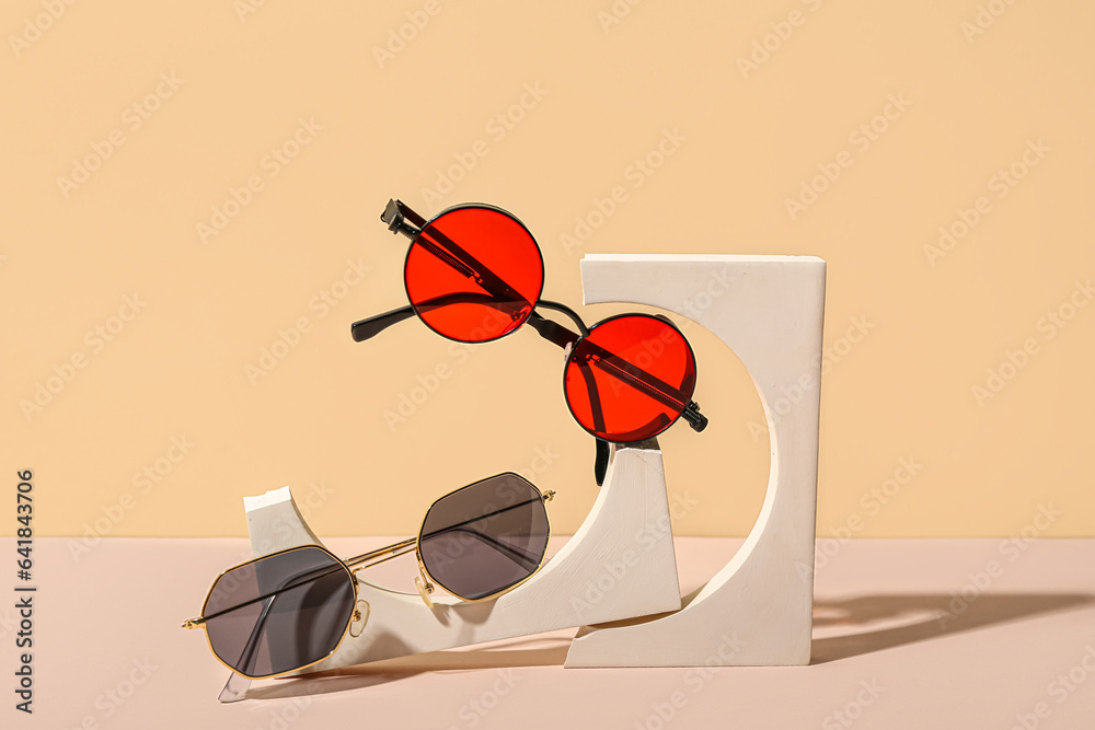 Decorative podiums with stylish sunglasses on beige background