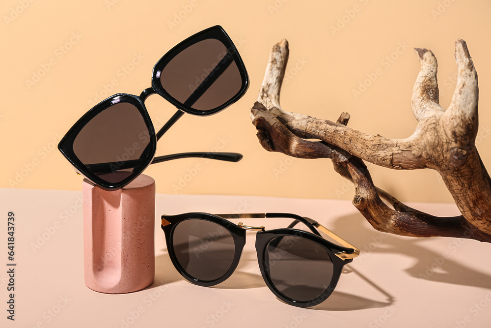 Decorative podium with stylish sunglasses and tree branch on beige background