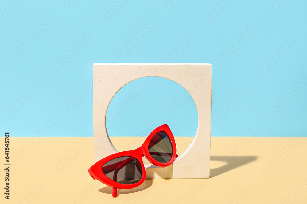 Decorative podium with stylish sunglasses on yellow table