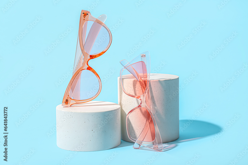 Decorative podiums with stylish sunglasses on blue background