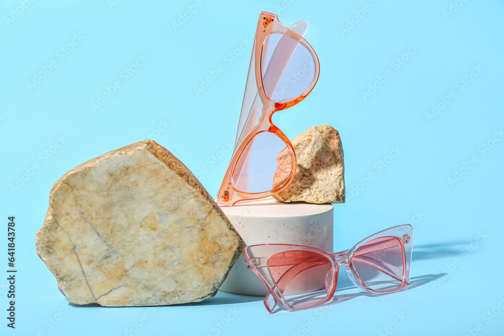 Decorative podium and stones with stylish sunglasses on blue background